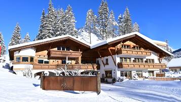 Een groot houten landhuis met meerdere balkons en besneeuwde bomen op de achtergrond.