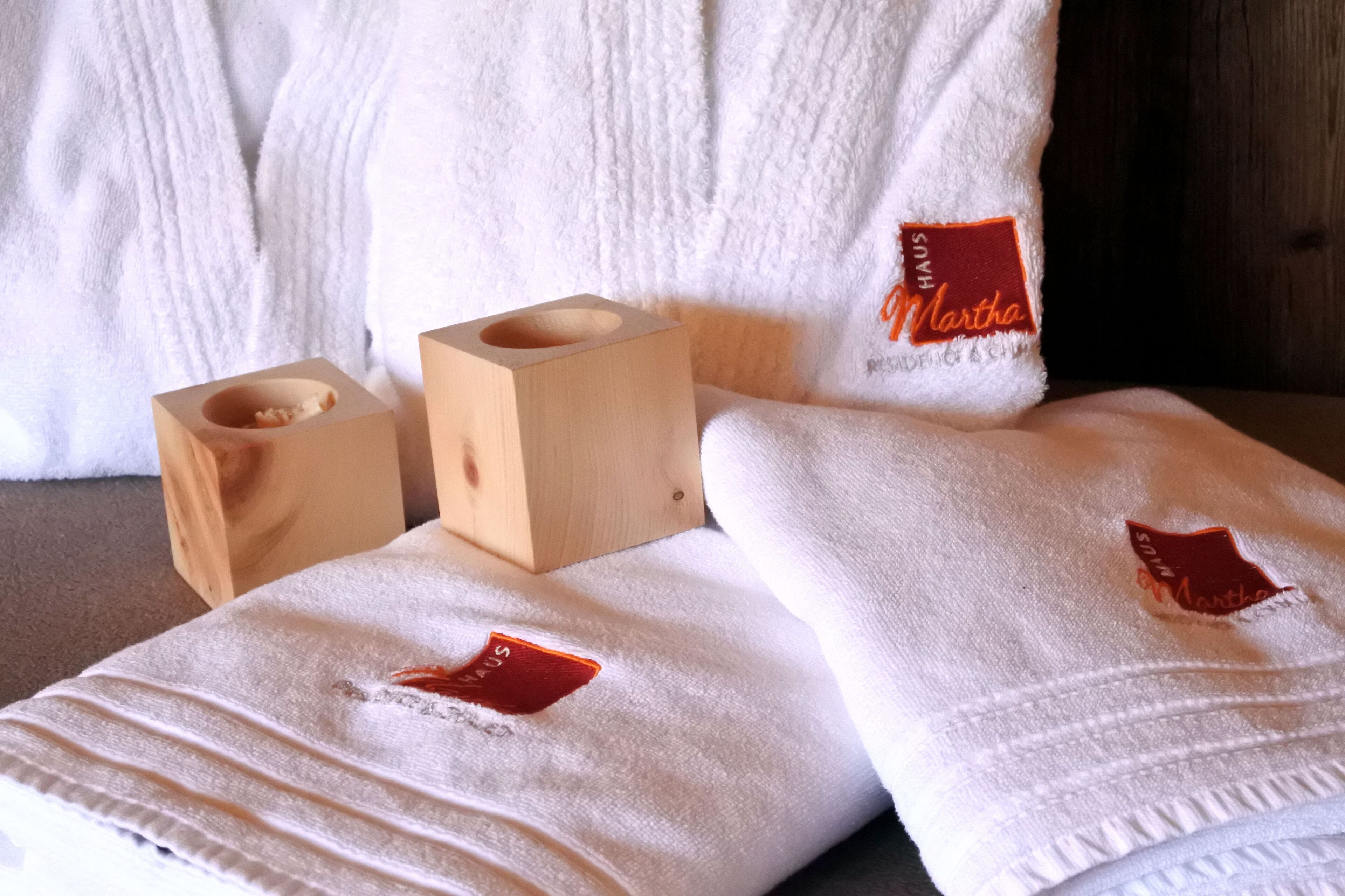Neatly folded white towels with red labels on a bed, a wooden tissue box, and a white textured pillow.