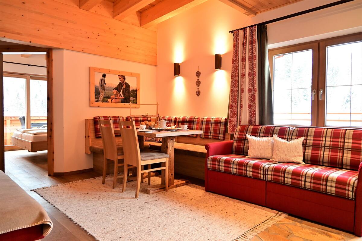 Une pièce chaleureuse avec un plafond en bois, un canapé à carreaux, une table à manger avec des chaises et un tableau accroché au mur.