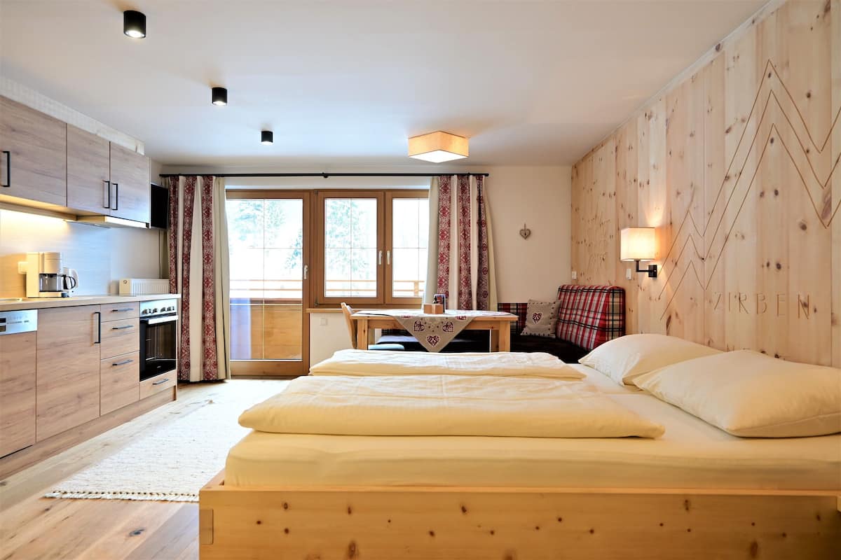 Une chambre moderne avec un lit en bois, une petite table et un coin cuisine.