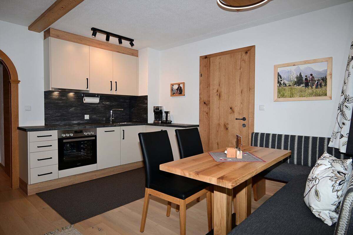 Une cuisine compacte avec une table et des chaises en bois, un four encastré et un coin repas avec un banc.