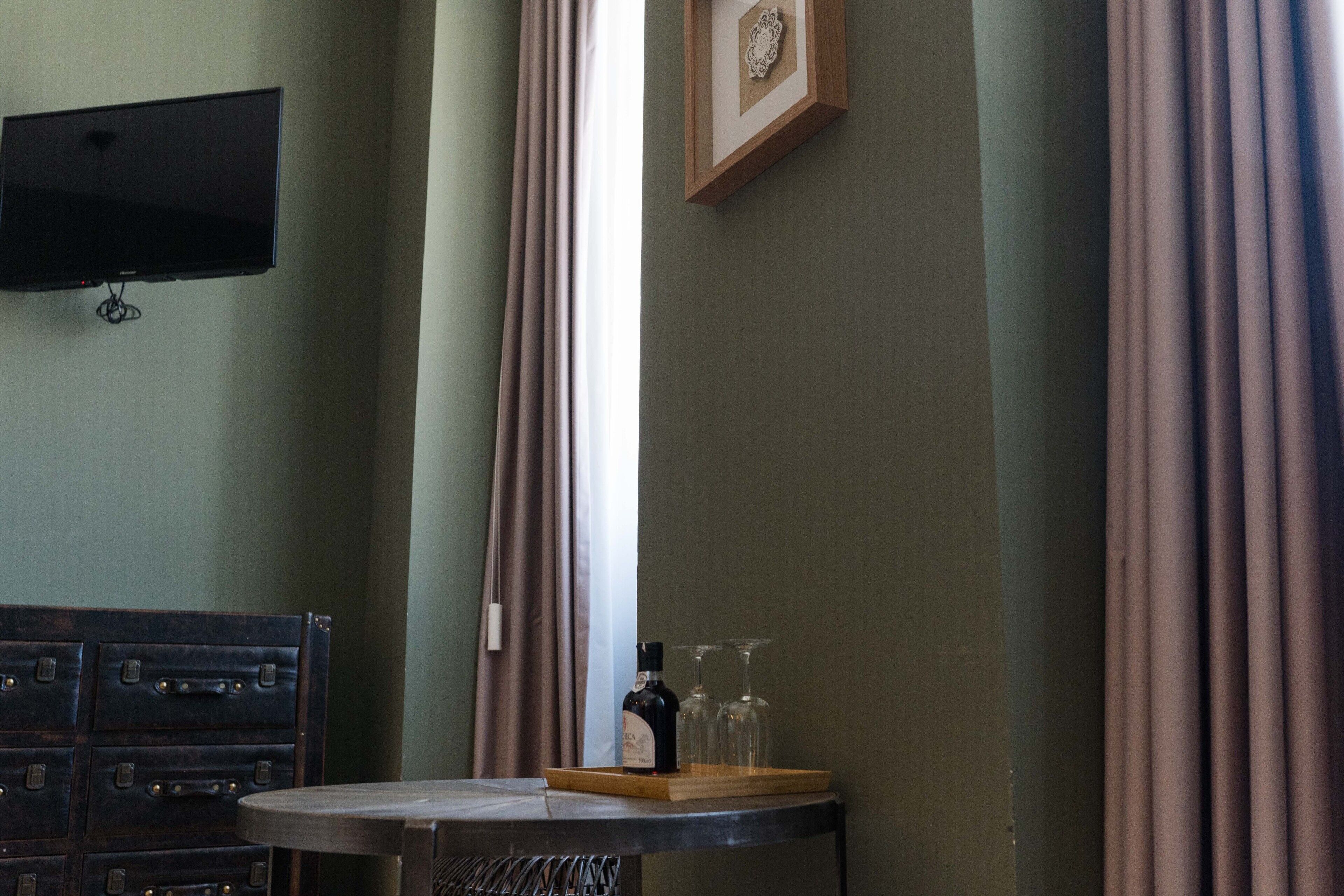 Una habitación con una televisión de pantalla plana montada en la pared, una pequeña mesa redonda con una botella y vasos, y un mueble de madera oscura.