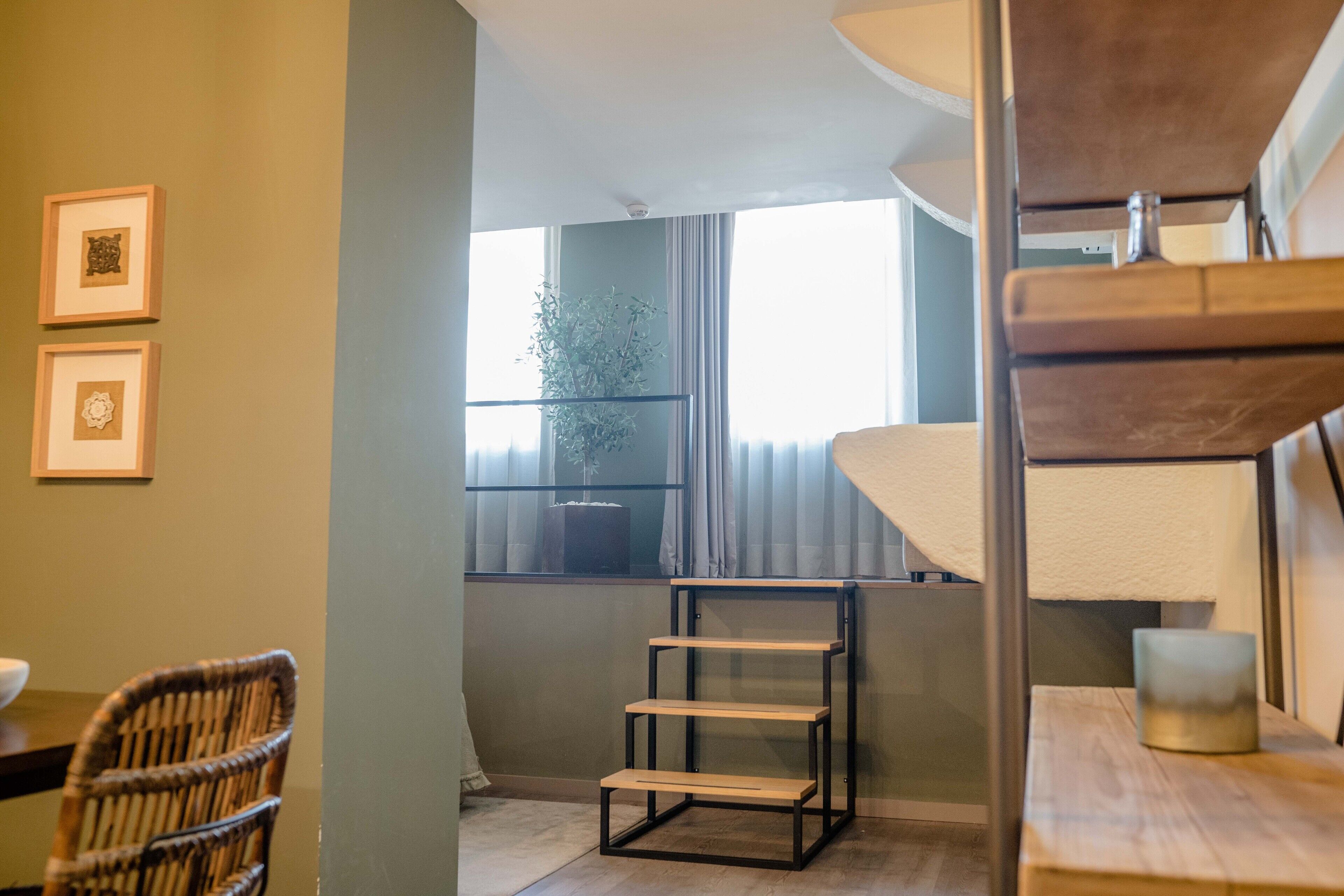 A room with a wooden dining table, a wicker chair, a metal shelf unit, and a window with curtains.