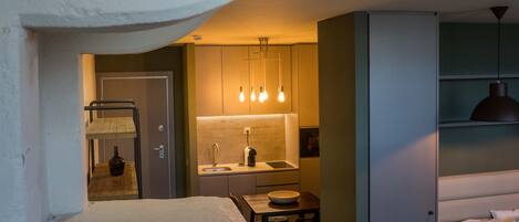 A compact hotel room with a bed, a small kitchenette, a dining area, and a separate sleeping area with a sofa.