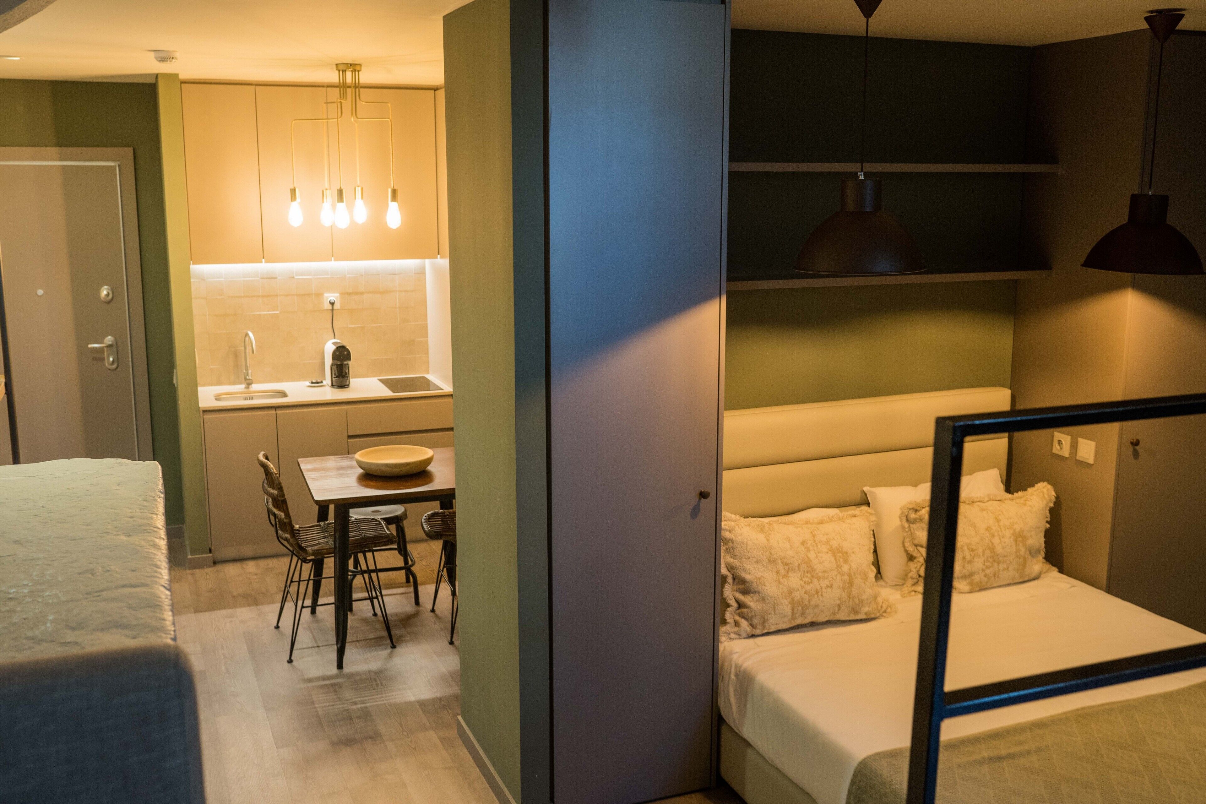 A compact hotel room with a kitchenette, a dining area, and a bed.