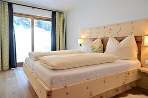 A bedroom with a wooden bed frame, two bedside lamps, and a view of a snowy landscape through the window. - Residence Martha (Biberwier)