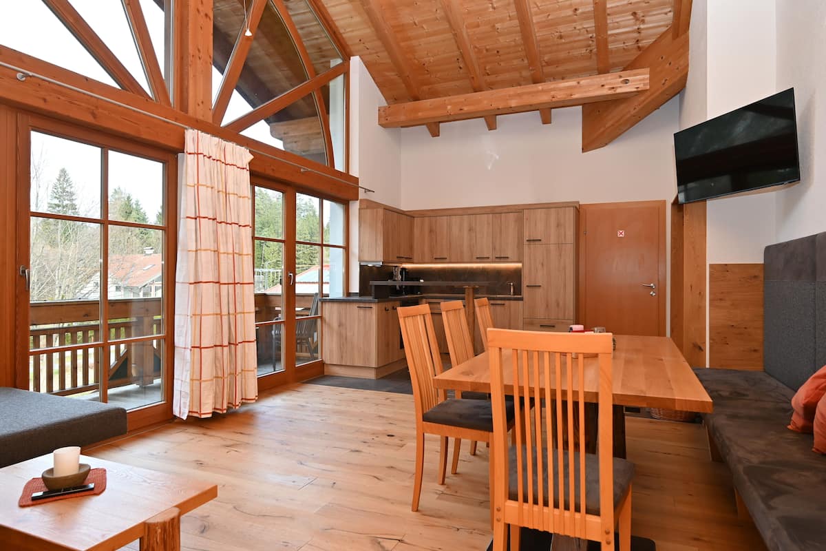 A spacious living area with a wooden dining table and chairs, a sofa, and a kitchen area with wooden cabinets and a built-in oven.