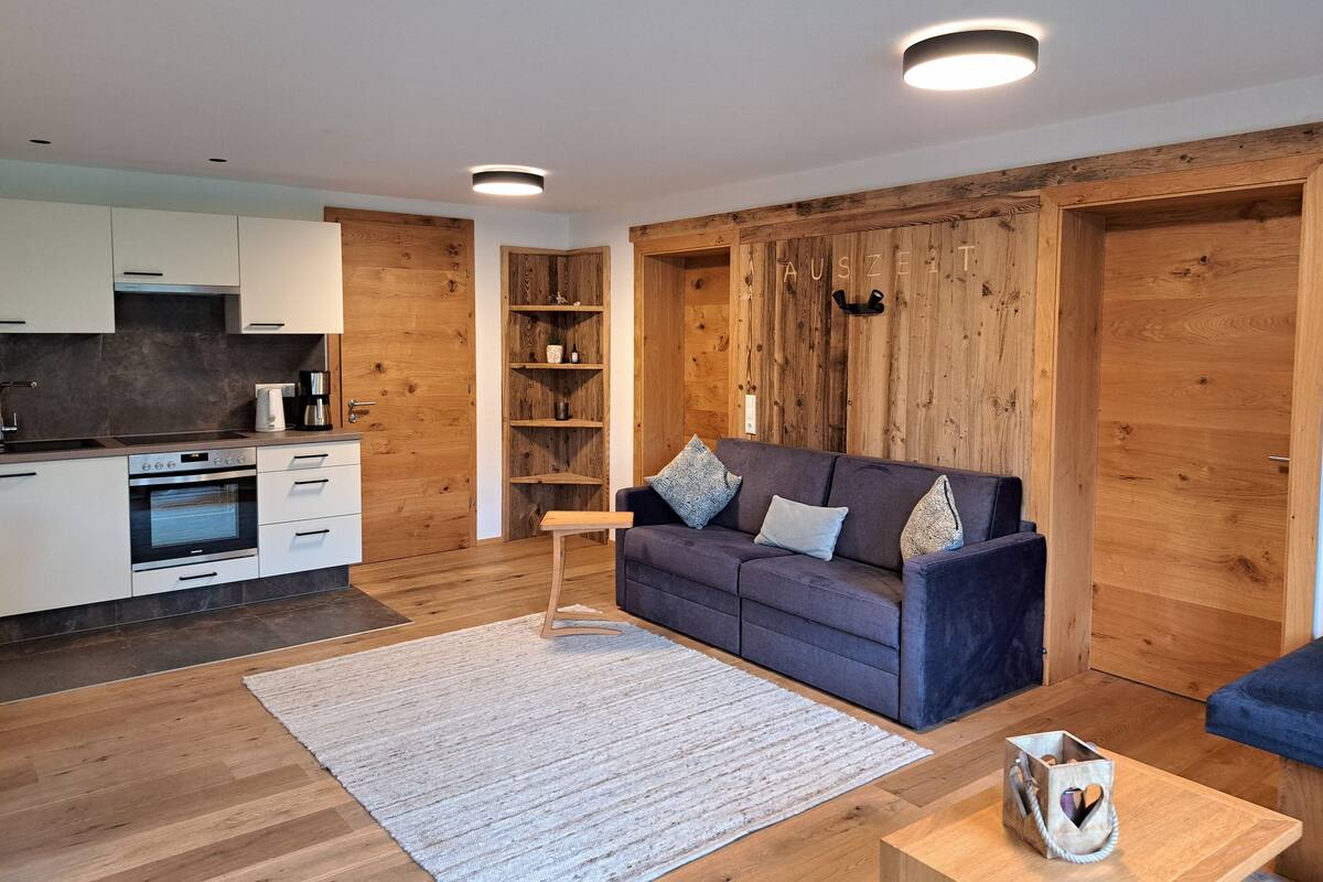 A modern living space with a kitchen, wooden walls, a sofa, and a coffee table.