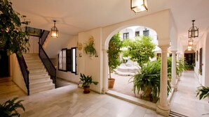 Un espace intérieur vaste et lumineux, agrémenté d’un escalier, de plantes en pot et offrant une vue sur un jardin extérieur.