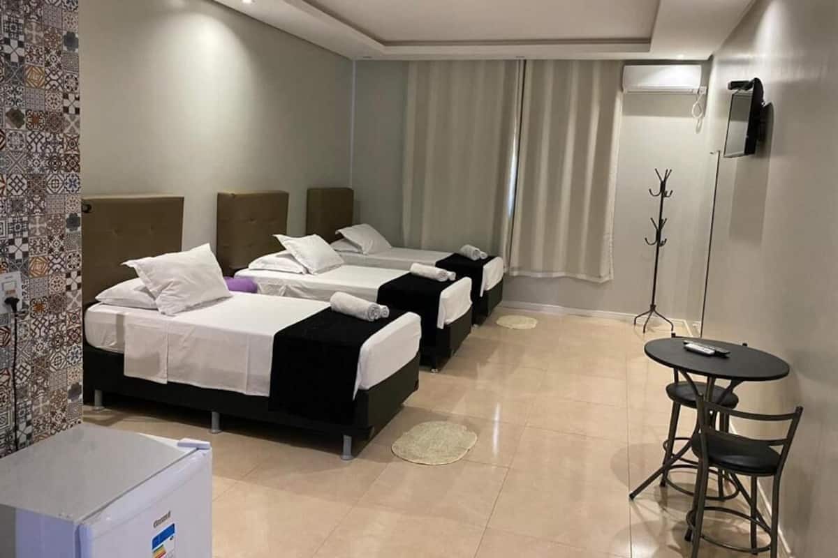 A hotel room with three beds, a small table, and a coat rack.