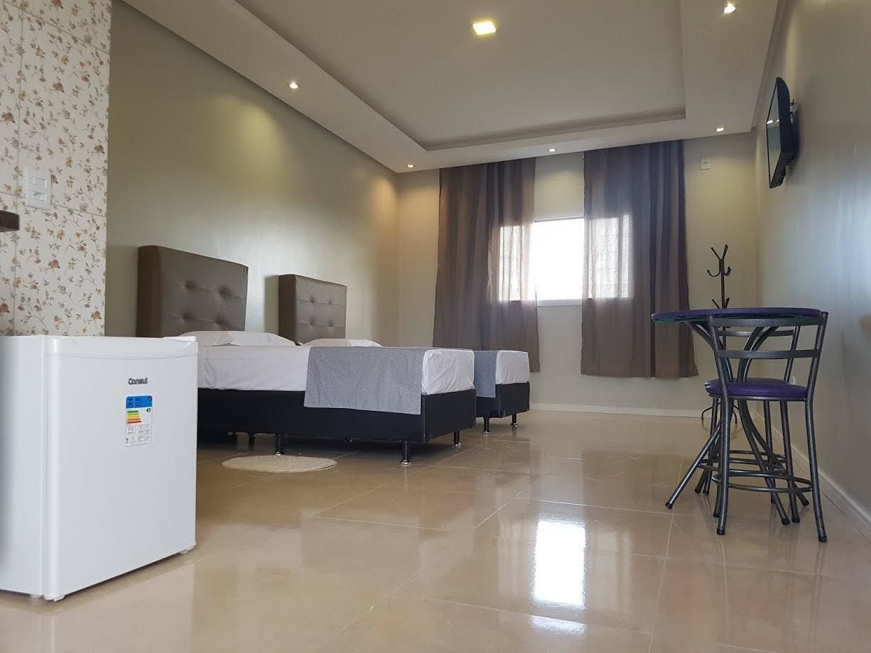 A hotel room with a bed, a refrigerator, a chair, and a television on the wall.