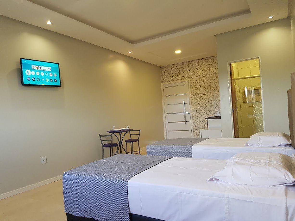 A hotel room with two beds, a desk with chairs, a TV mounted on the wall, and a door leading to a bathroom.