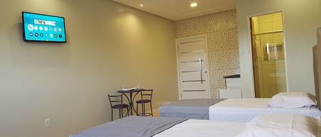 A hotel room with two beds, a desk with chairs, a TV mounted on the wall, and a door leading to a bathroom.