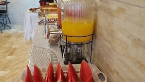 A buffet setup with a fruit bowl, watermelon slices, and a juice dispenser. - Pousada Aurora (Alto Paraíso de Goiás)