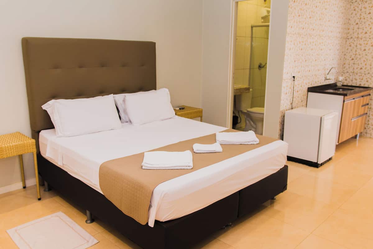 A neatly made bed with white linens, a brown headboard, and a small bedside table with a lamp.