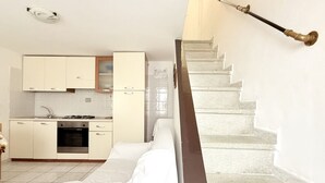 A kitchen with white cabinets, a stove, and a refrigerator. There is a staircase with a brass handrail leading to a landing. - N079 - Numana, delightful sky-earth in the historic center (Numana)