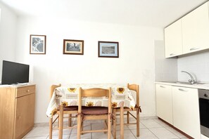Une petite cuisine avec une table à manger, des chaises, un téléviseur et des tableaux encadrés accrochés au mur.