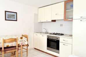 Une cuisine de taille réduite avec des meubles blancs, une cuisinière à gaz, un four et une table à manger avec des chaises.