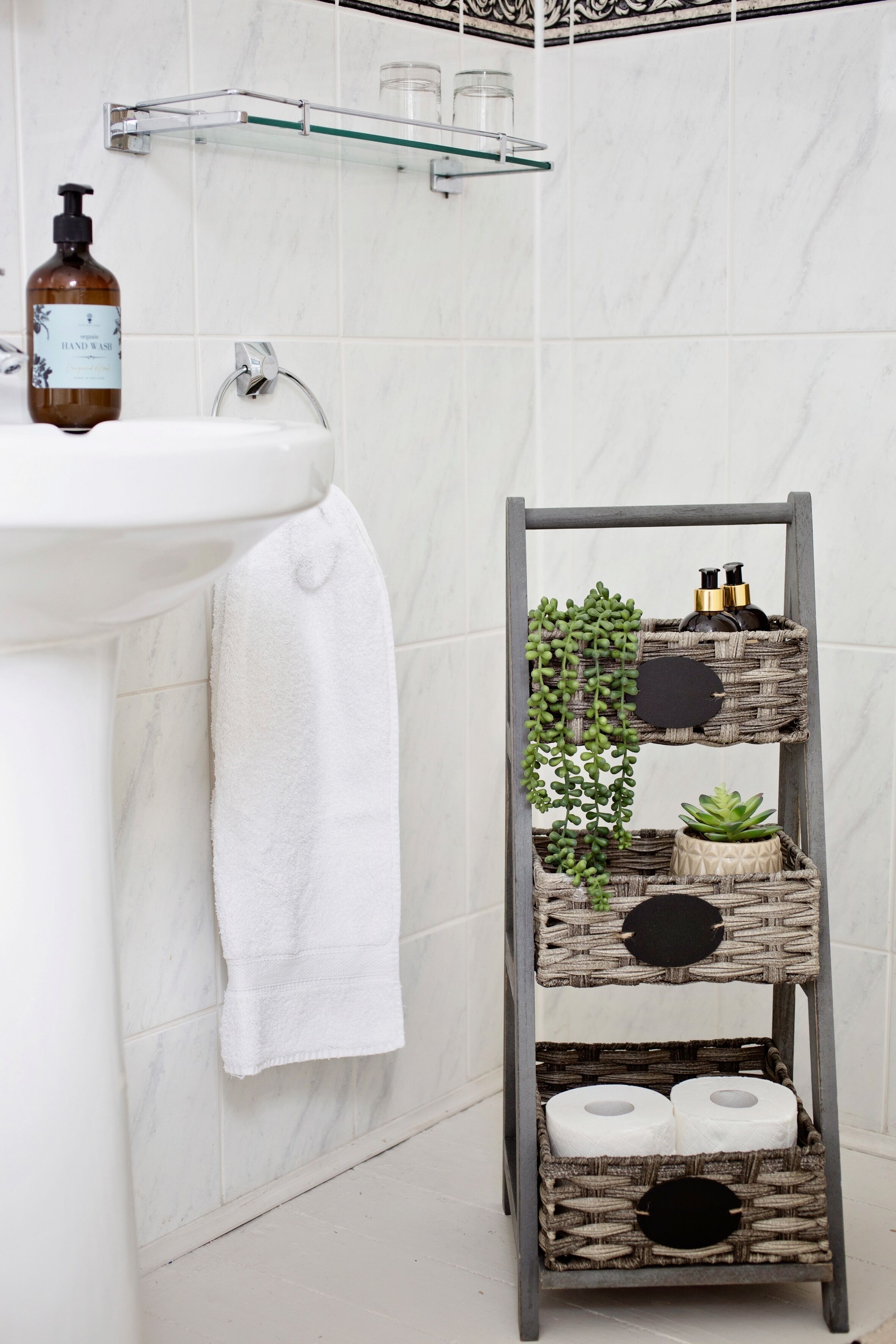 A bathroom with a white sink, a towel hanging on the wall, and a wooden shelf with toiletries and plants.