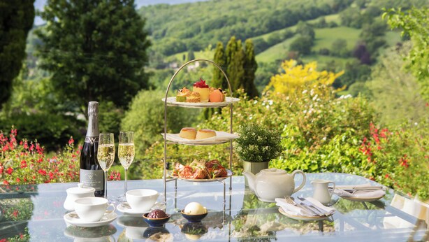 Une table dressée pour un service à thé, avec un présentoir à étages contenant des pâtisseries et des sandwichs, une bouteille de vin et des tasses à thé.