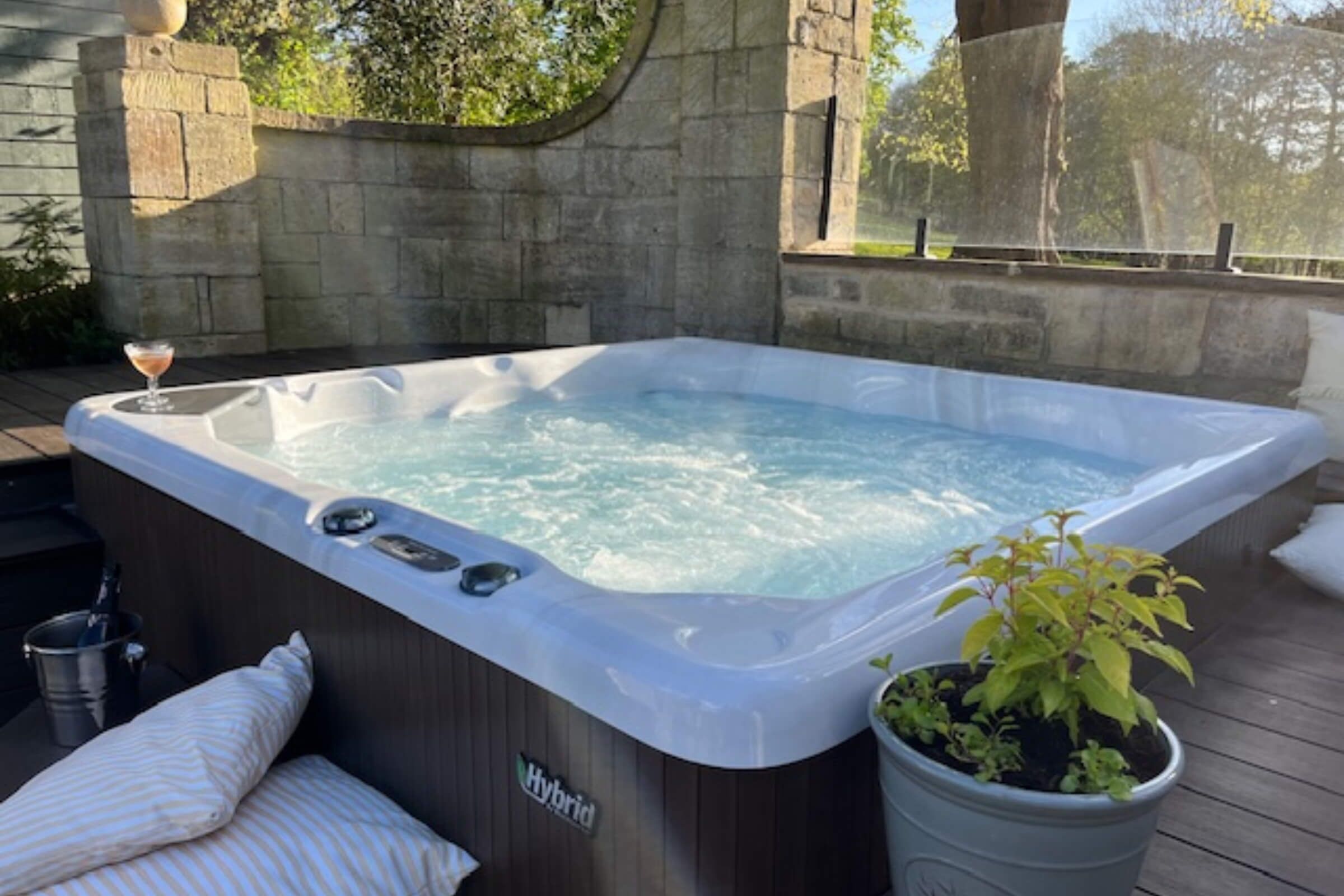 A hot tub with a "Hybrid" label, a potted plant, and a stone wall in the background.