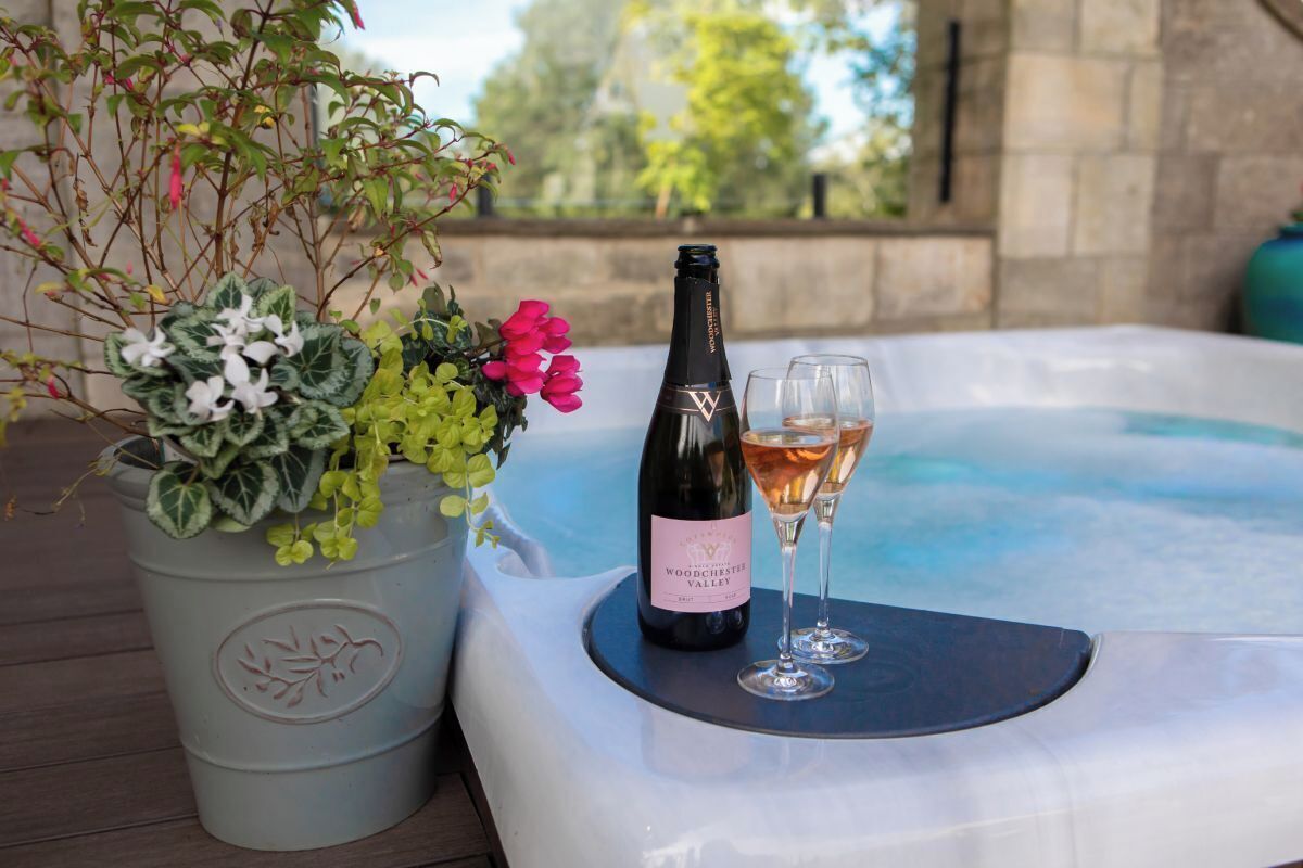 A hot tub with a bottle of wine and two glasses on a table, surrounded by potted plants.