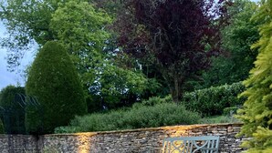 Un mur de pierre agrémenté d’un banc et de lanternes, dans un jardin où poussent des fleurs blanches.