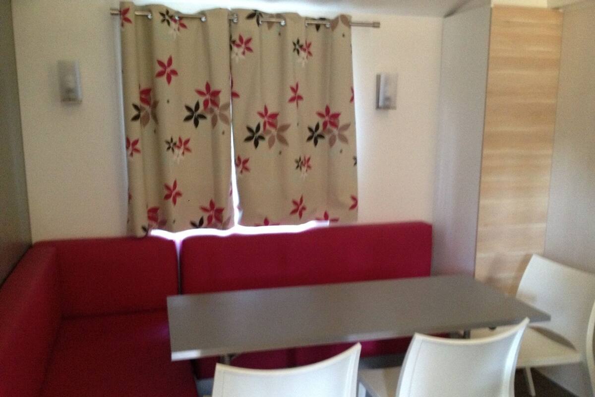 Une pièce avec un canapé rouge, une table et deux chaises blanches.