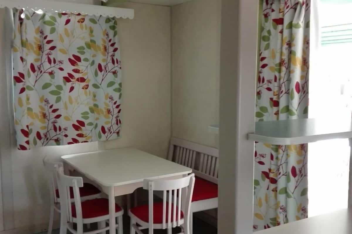 Un coin repas avec une table et des chaises blanches, un banc et des rideaux à motifs floraux.