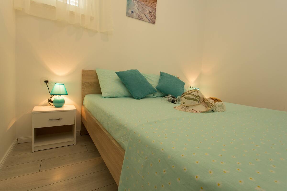 A bedroom with a bed, a nightstand, a lamp, and a wall-mounted painting.