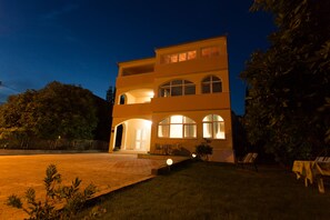 A two-story building with a symmetrical facade, large arched windows, and a well-lit entrance. - Apartments Kampanel (Kastela)