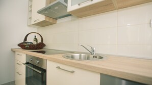 A modern kitchen with a stainless steel sink, wooden countertop, built-in oven, and a basket with a bottle. - Apartments Kampanel (Kastela)