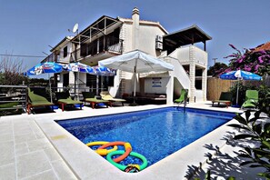 A swimming pool with lounge chairs and umbrellas, a building with a balcony, and a sign for Heineken. - Villa Martini (Marina)