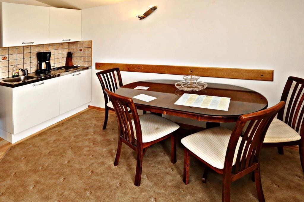 A dining area with a wooden table and chairs, a kitchen with white cabinets and a coffee maker, and a light fixture on the wall.