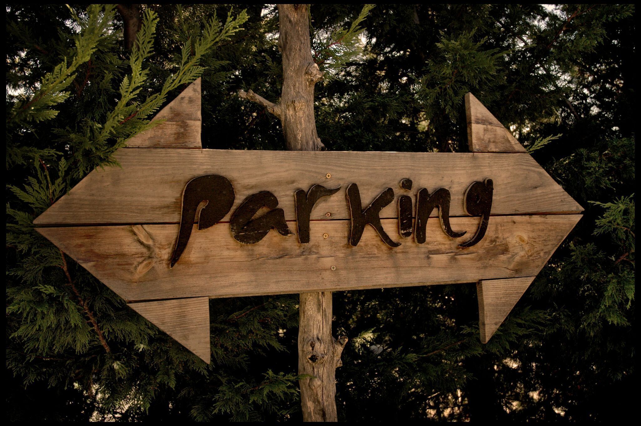 A wooden arrow sign with the word "Parking" carved into it, pointing to the right.