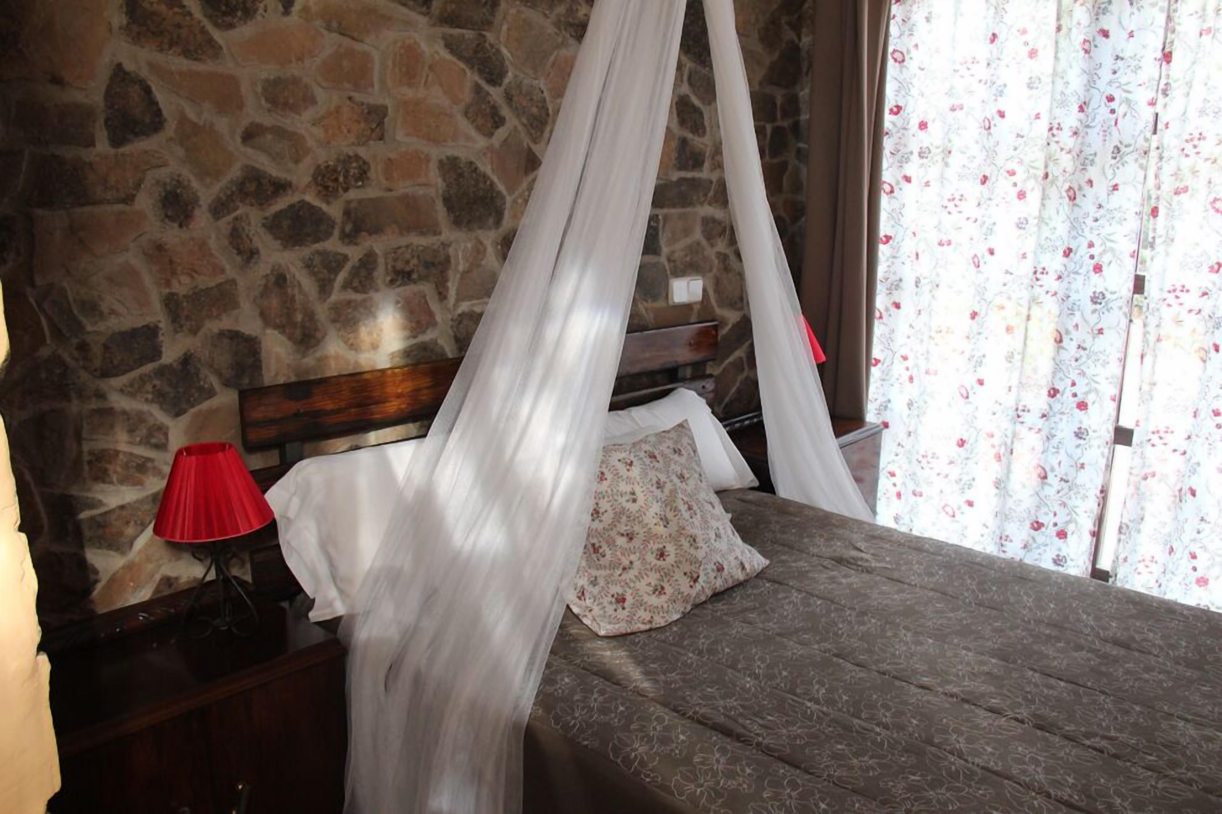 Ein Schlafzimmer mit Steinwand, Himmelsbett, roter Lampe und blumigen Vorhängen.
