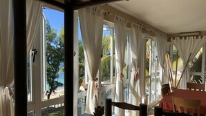 Ein Zimmer mit großen Fenstern, einem Holztisch und Blick auf einen Strand und Palmen.