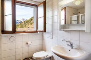 A bathroom with a toilet, sink, and a window with a mountain view. - Alpine Apartment With Stunning Views (Chateau-d'Oex)