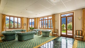 A spacious room with a green patterned carpet, a large window with a mountain view, and a green sofa set. - Alpine Apartment With Stunning Views (Chateau-d'Oex)