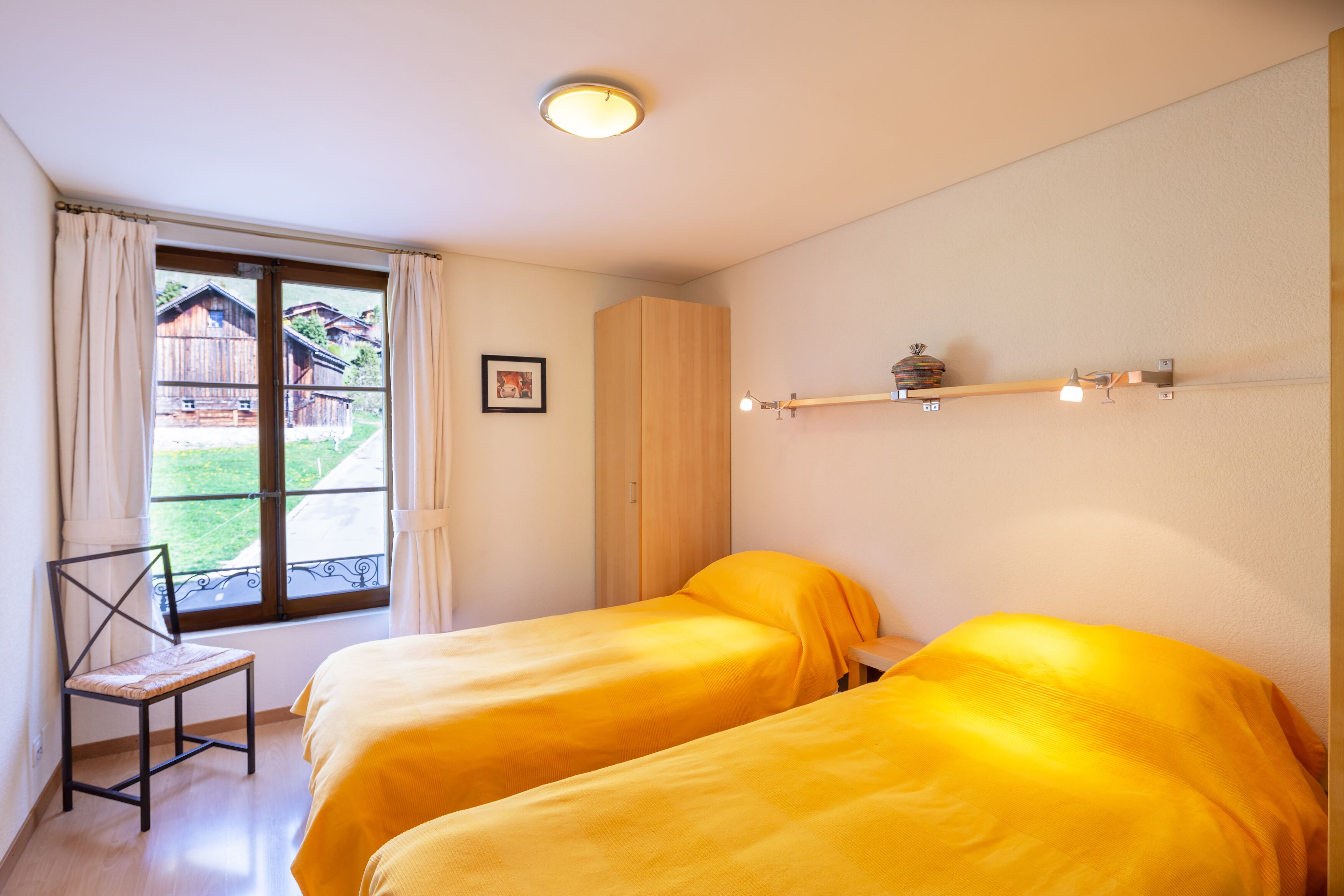 Quarto com duas camas, janela com cortinas, guarda-roupa de madeira e uma estante com luzes.