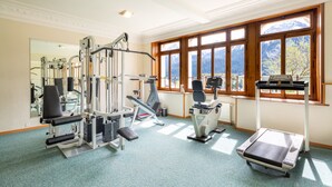 A gym with various exercise equipment, large windows with a mountain view, and a mirror on the wall. - Alpine Apartment With Stunning Views (Chateau-d'Oex)