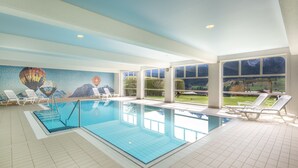 An indoor swimming pool with clear blue water, white tiled floors, and a mural of a hot air balloon on the wall. - Alpine Apartment With Stunning Views (Chateau-d'Oex)