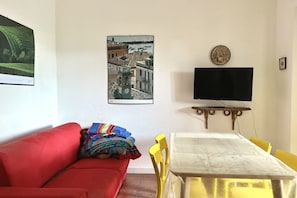 A living room with a red sofa, a table with yellow chairs, a flat-screen TV, and a framed picture on the wall.