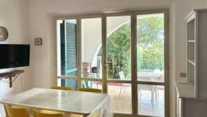 A room with a dining table, chairs, a television, and a sliding glass door leading to an outdoor patio with chairs and a table. - N106 - Numana, villa with garden and right sea view (Numana)