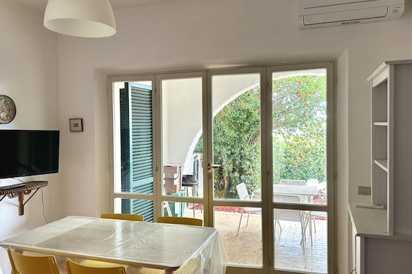 A room with a dining table, chairs, a television, and a sliding glass door leading to an outdoor patio with chairs and a table.