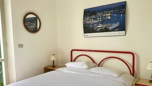 A bed with a red metal frame, white bedding, a nightstand with a lamp, a framed picture of a cityscape, and a mirror on the wall. - N106 - Numana, villa with garden and right sea view (Numana)