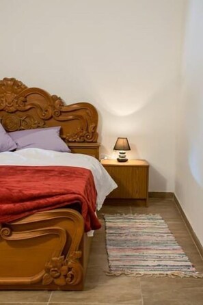 A bedroom with a wooden bed, a nightstand with a lamp, and a colorful rug.