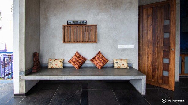 Un banc avec des coussins et un panneau en bois, dans une pièce dont le mur est en béton et la porte en bois.