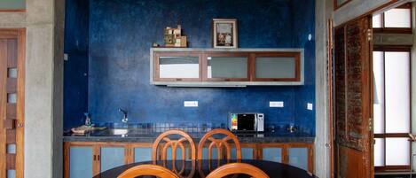A kitchen with a blue wall, wooden cabinets, a microwave, and a dining table with chairs.