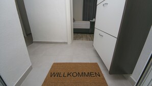 A hallway with a welcome mat, a bed, and a wardrobe.